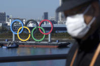 FILE - In this Dec. 1, 2020, file photo, a man wearing a protective face mask to help curb the spread of the coronavirus walks with the Olympic rings in the background in the Odaiba section in Tokyo. Opposition to the Tokyo Olympics is growing with calls for a cancellation as virus cases rise in Japan. The International Olympic Committee and local organizers have already said another postponement is impossible, leaving cancellation, or going ahead, as the only options. (AP Photo/Eugene Hoshiko, File)