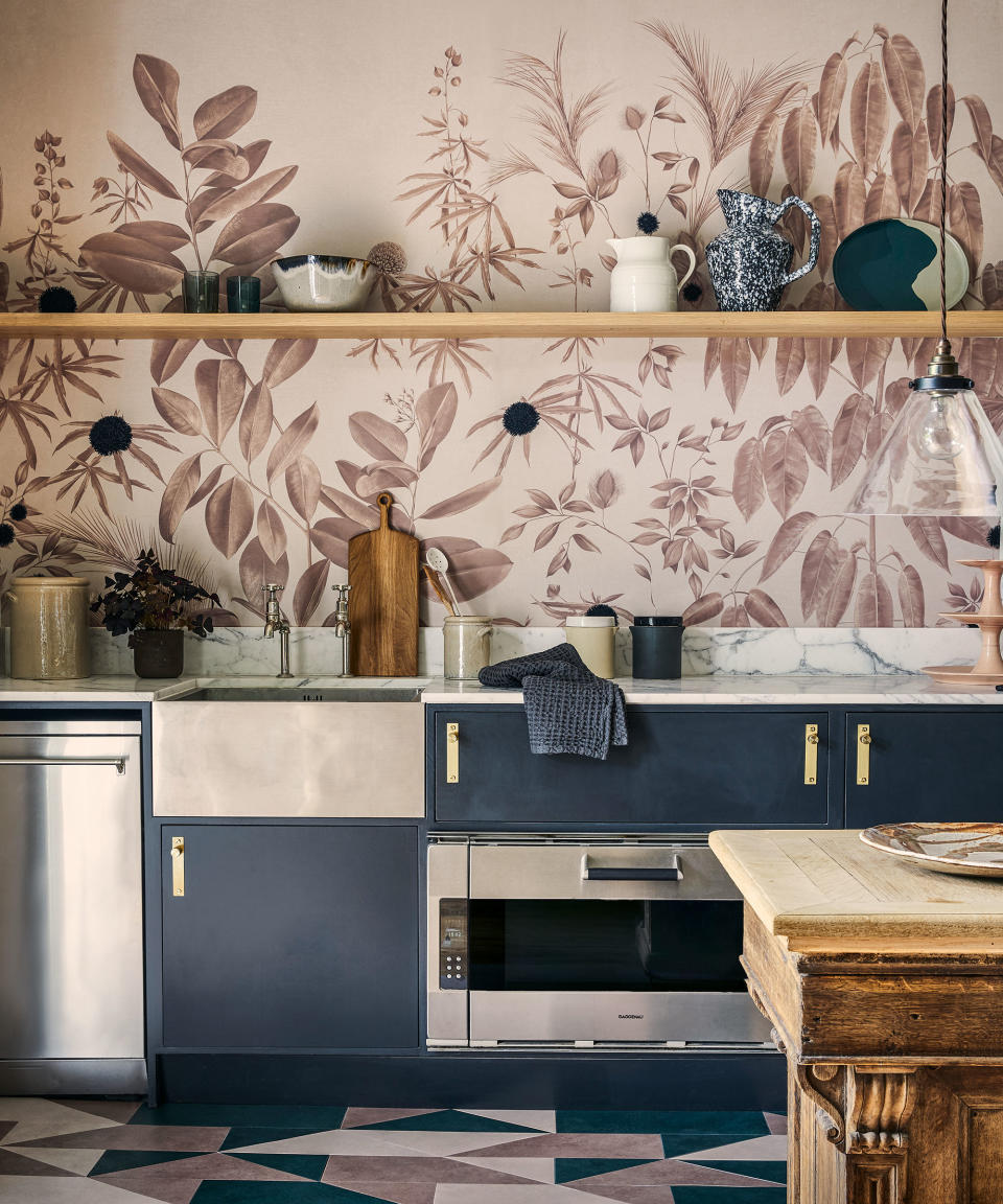 A beige oversized botanical print wallpaper in a kitchen with open shelving and a wooden table.