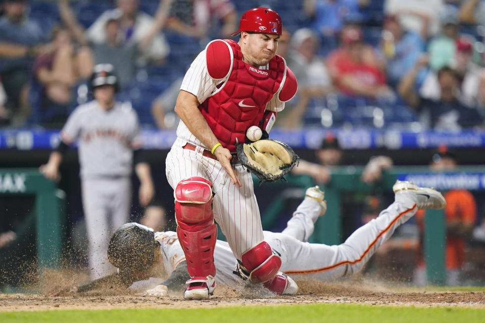 San Francisco Giants' Wilmer Flores, left, scores past Philadelphia Phillies catcher J.T. Realmuto on a single by Joc Pederson during the 10th inning of a baseball game, Tuesday, May 31, 2022, in Philadelphia. (AP Photo/Matt Slocum)