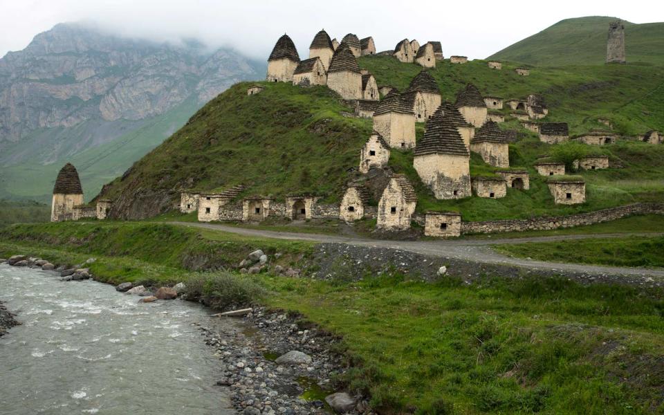 <p>In the state of North Ossetia-Alania, near Russia’s border with Georgia, is a charming village with modest stone houses that dot the foothills. Known as the city of Dargavs, this idyllic hamlet in a Caucasus Mountain ridge is home only to the dead. The homes are crypts filled with the bones of the surrounding city’s departed residents, buried with all their clothes and personal belongings. Known as the City of the Dead (title that dates <a rel="nofollow noopener" href="https://www.rt.com/shows/russia-close-up/ancient-ossetia-dead-city/" target="_blank" data-ylk="slk:back to the 14th- century;elm:context_link;itc:0;sec:content-canvas" class="link ">back to the 14th- century</a>) locals warn that visitors to the necropolis are cursed. </p>