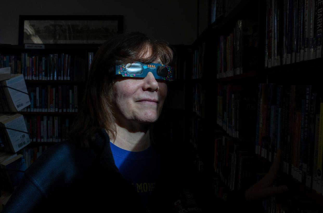 Becky Poca, a library clerk with the Rasey Memorial Branch Library, or as many locals know it as Luna Pier Library, wears a pair of solar eclipse glasses inside the library on Thursday, March 7, 2024.