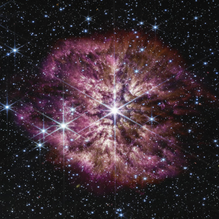 Wolf-Rayet 124, center, surrounded by billowing cloud formations of debris, dominates the image, with a half-dozen smaller stars arrayed around it. 