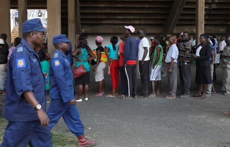 Police officers walk past mourners as they queue to pay their last respects to Former Zimbabwean president Robert Mugabe as he lies in state at the at Rufaro stadium