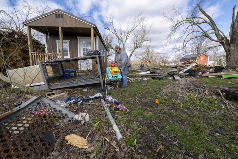 Misty Grimes, searches through debris scattered throughout her yard left from a late-night tornado in Sullivan, Ind., Saturday, April 1, 2023. Grimes and her husband, Matt, were home as the storm hit, and found shelter inside their home. Neither were injured. Multiple deaths were reported in the area following the storm. (AP Photo/Doug McSchooler)