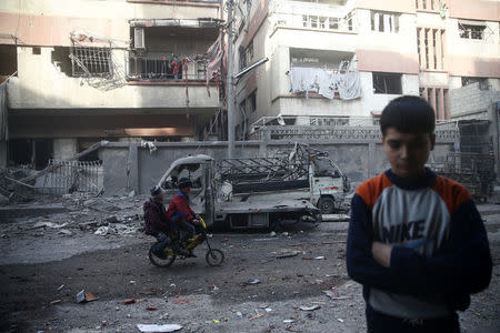 Children ride on a bicycle at a damaged site after an airstrike in the besieged town of Douma, Eastern Ghouta, Damascus, Syria February 9, 2018. REUTERS/Bassam Khabieh