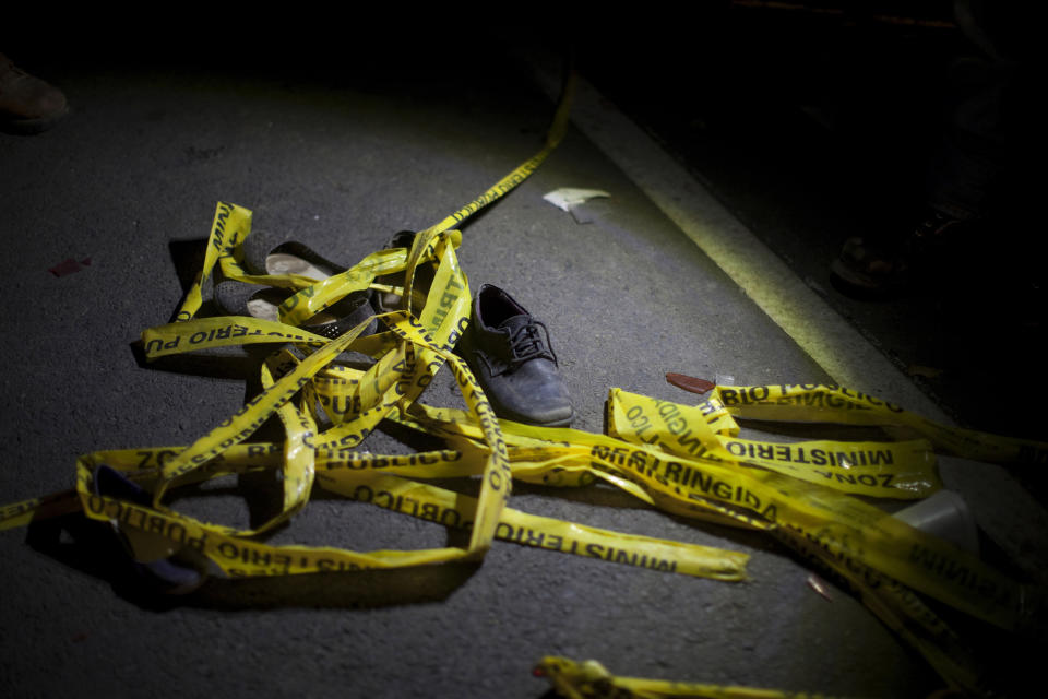 In this March 28, 2019 photo, yellow police tape and a shoe lay on the ground in the place where an accident occurred, in Nahuala, Guatemala. A large truck slammed into a crowd gathered on a dark highway in western Guatemala, killing over a dozen people and leaving bodies scattered on the roadway, firefighters said. (AP Photo/Sandra Sebastian)