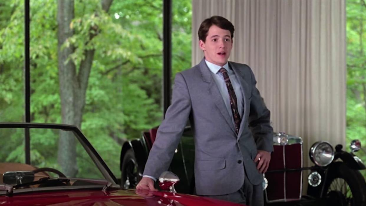  Matthew Broderick as Ferris Bueller standing next to the red sports car 