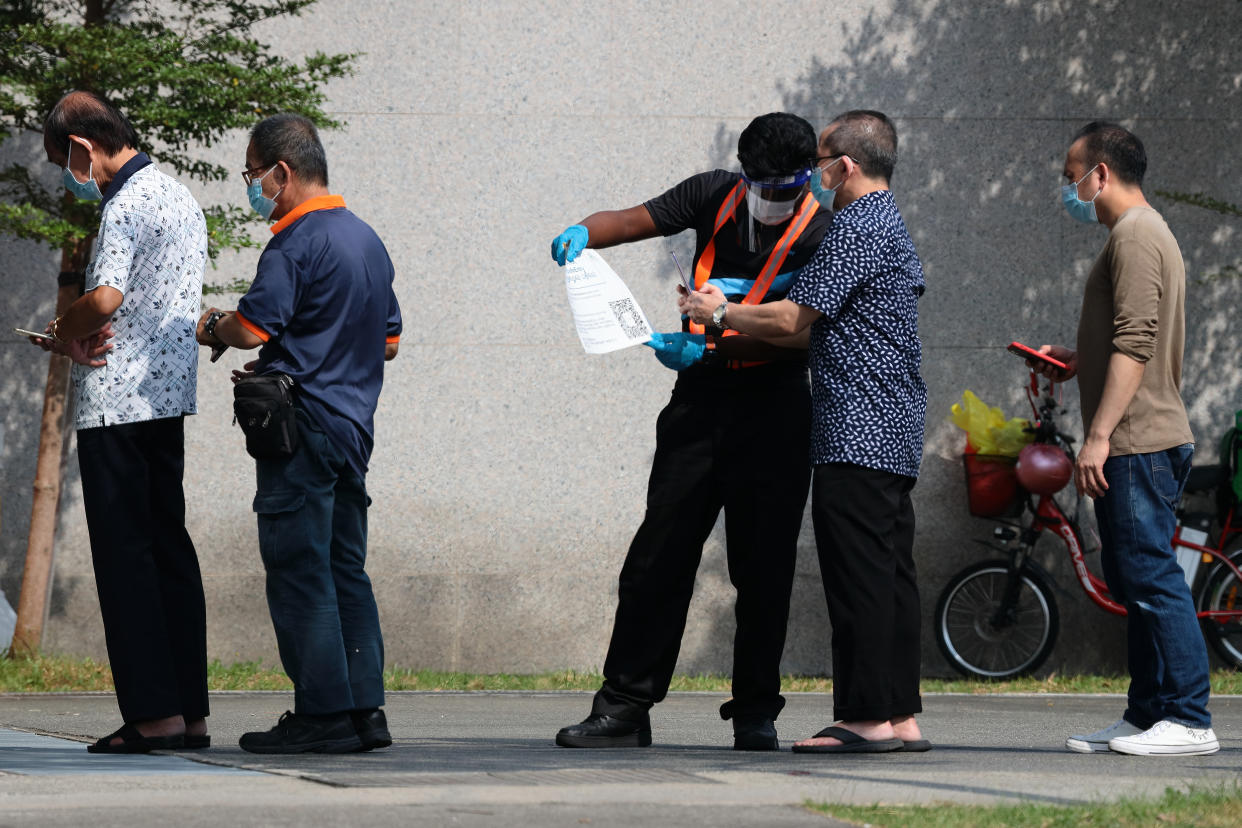 An officer wearing glove, face shield and face mask conducts safe entry check-in for people waiting in queue to take their COVID-19 antigen rapid test outside a quick test centre on October 16, 2021 in Singapore. (Photo by Suhaimi Abdullah/NurPhoto via Getty Images)