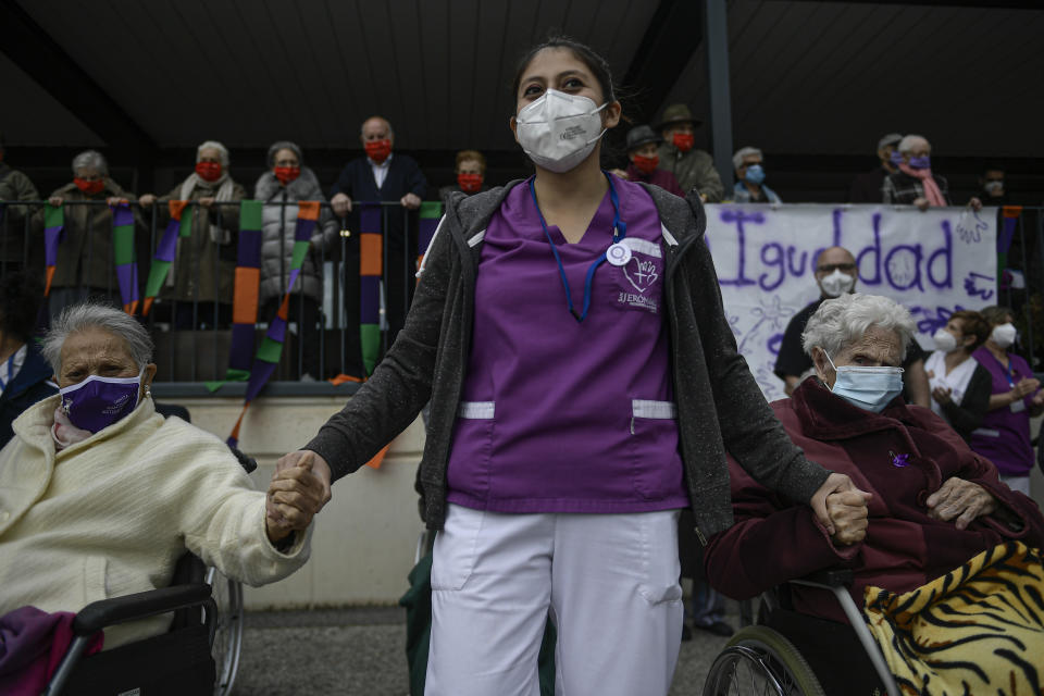 A health worker at San Jeronimo nursing home, wearing mask protection, holds hands with two elderly women while while taking part during International Women's Day in Estella, around 38 kms (23 miles) from Pamplona northern Spain, Monday, March 8, 2021. Many small-sized events are taking place across Spain creatively organized to prevent gatherings that could trigger a new spike of coronavirus contagion. (AP Photo/Alvaro Barrientos)