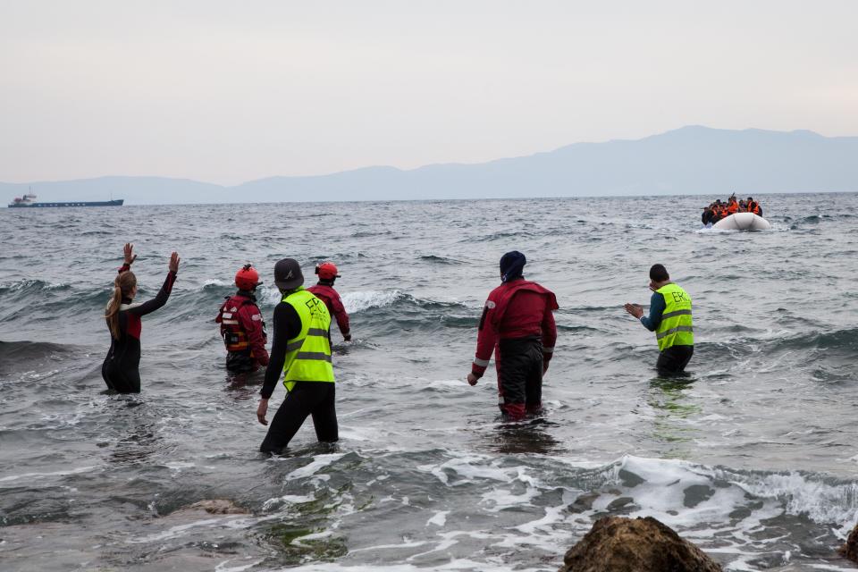 People hail a dinghy as it arrives to Lesbos on March 22, 2016.