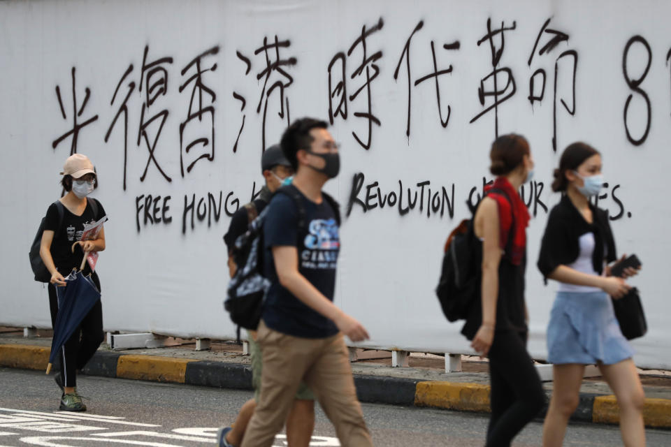 Protesters walk past a wall with spray-painted slogans during a demonstration in Hong Kong, Saturday, Aug. 3, 2019. Hong Kong protesters ignored police warnings and streamed past the designated endpoint for a rally Saturday in the latest of a series of demonstrations targeting the government of the semi-autonomous Chinese territory. (AP Photo/Vincent Thian)
