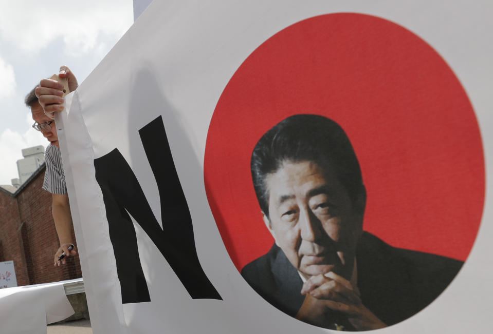 A South Korean man stands next to a sign with a picture of the Japanese Prime Minister Shinzo Abe during a rally to denounce Japan's trade restrictions on South Korea in Seoul, South Korea, Thursday, Aug. 8, 2019. (AP Photo/Lee Jin-man)