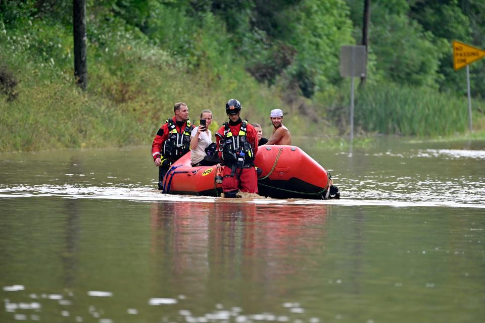 Rescue workers walk an inflatable boat across floodwaters with a woman inside.