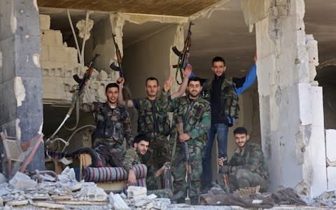 Syrian soldiers wave inside a destroyed building nearly a week after retaking the town of Harasta from the rebels, in Eastern Ghouta - Credit: AFP