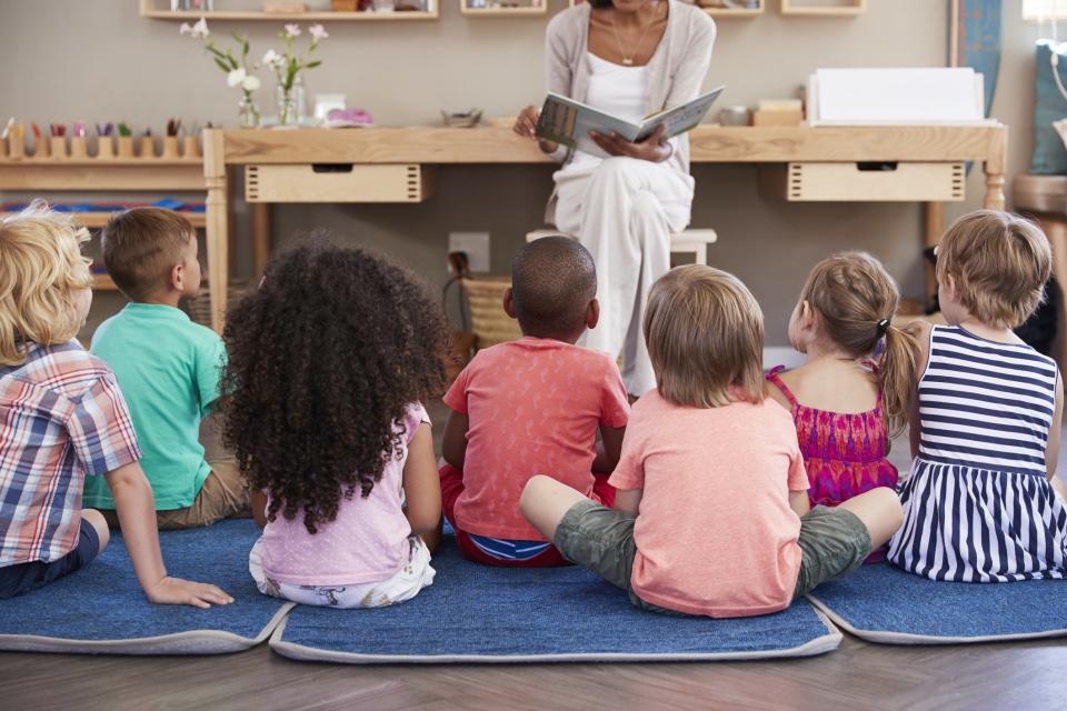 A group of children sitting on mats in a child care center listening to a story.