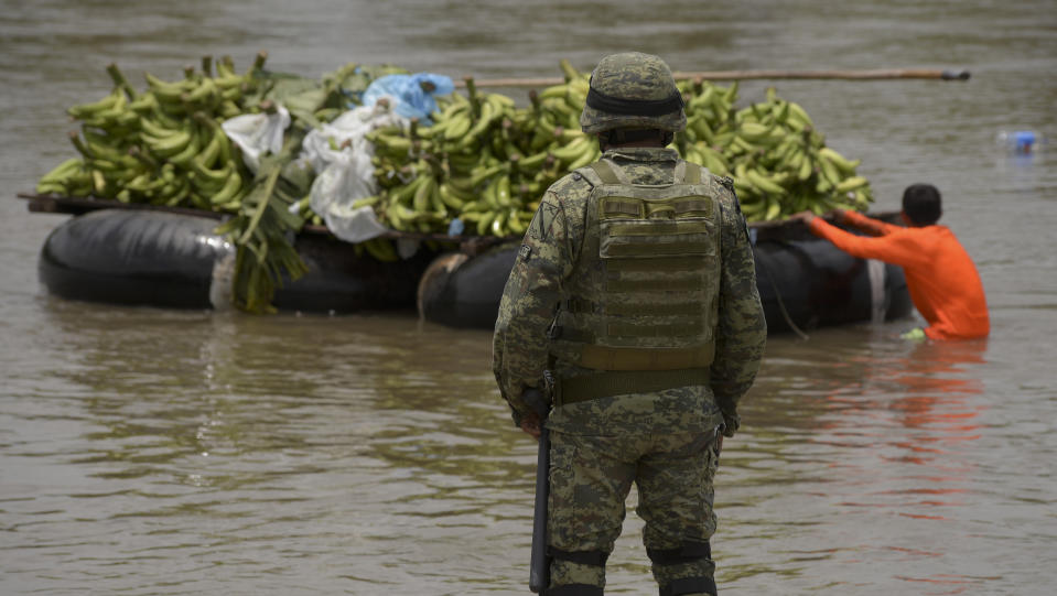 A soldier stands on the bank of the Suchiate River where a youth moves a load of bananas between Guatemala and Mexico, during a press tour organized by the National Guard near Ciudad Hidalgo, Mexico, Wednesday, July 3, 2019. A National Guard commander explained to the agents that they were there to support immigration enforcement, but not to interfere in the brisk and vital commerce carried out on rafts that shuttle all manner of goods between the two countries. (AP Photo/Idalia Rie)