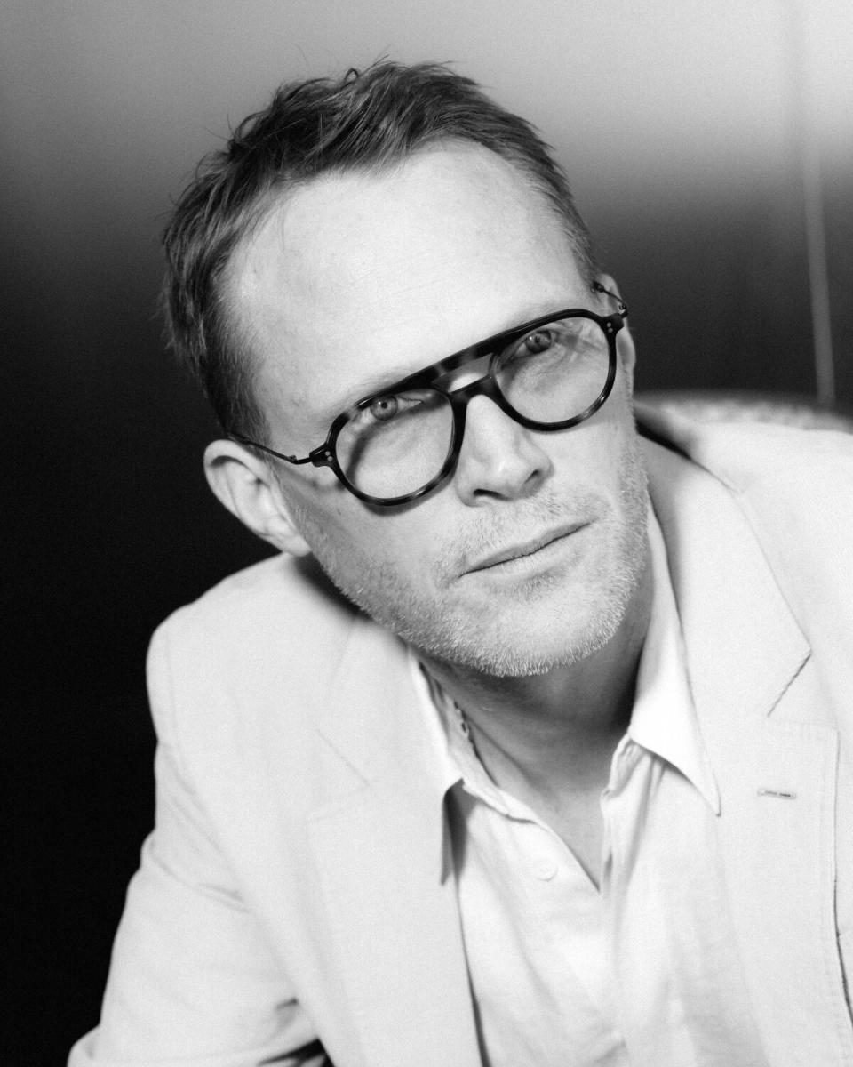 A man in a light-colored suit and black eyeglasses poses for a portrait.