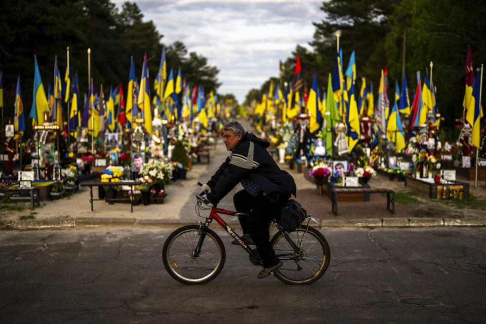 A man rides a bicycle past the tombs of Ukrainian soldiers killed during the war, at Lisove cemetery in Kyiv, Ukraine, Tuesday, April 23, 2024. (AP Photo/Francisco Seco)