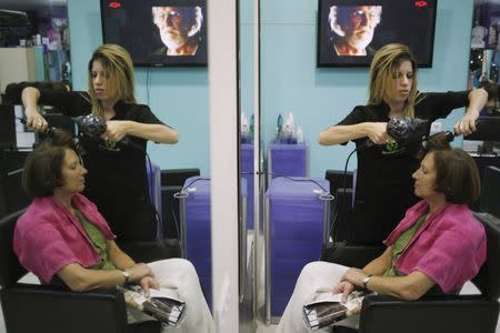 Desire Vargas, 20, is reflected in a mirror as she combs a customer's hair at a hairdressing salon where she studies a course in beauty and hairdressing in downtown Ronda, near Malaga, southern Spain, October 2, 2015. REUTERS/Jon Nazca