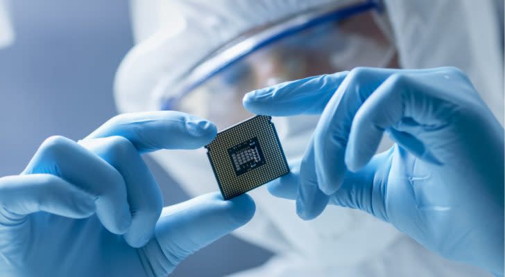 In Ultra Modern Electronic Manufacturing Factory Design Engineer in Sterile Coverall Holds Microchip with Gloves and Examines it.