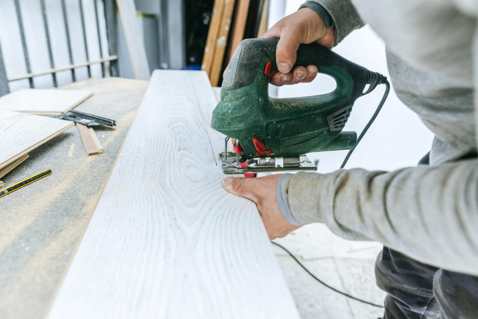 Person using an electric jigsaw to cut a wooden plank on a workbench