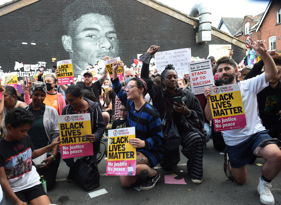 Manifestantes se arrodillan mientras sostienen pancartas en contra del racismo frente al mural del jugador inglés Marcus Rashford. (Foto: Reuters)