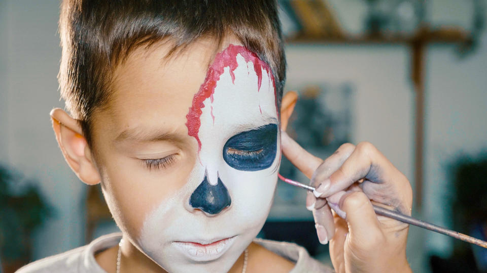 Make-up artist makes the boy halloween make up. Halloween child face art. Drawing skull body art for halloween party.