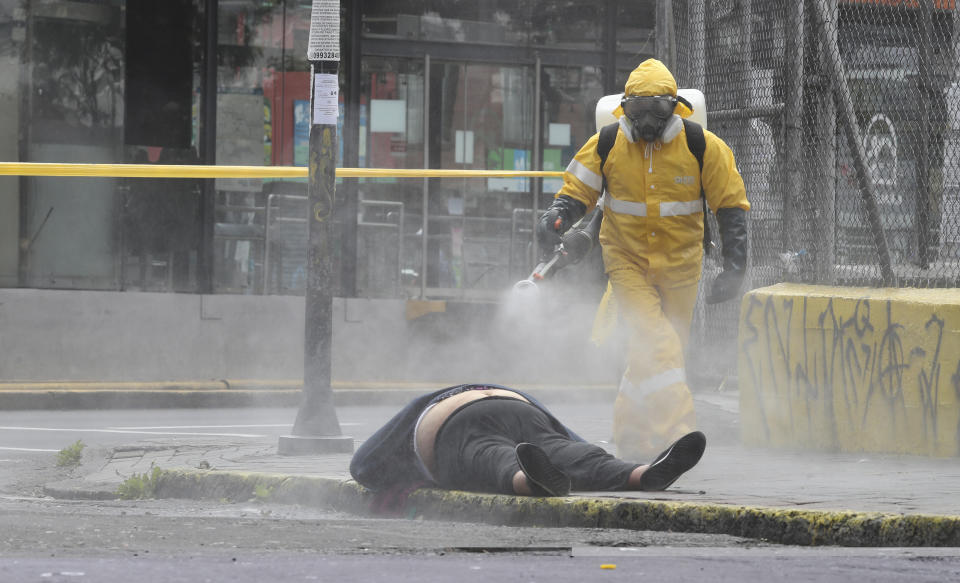 FILE - A worker from the city's forensic department sprays disinfectant over the body of a woman who died on a street in Quito, Ecuador, Thursday, May 14, 2020. Forensic workers at the scene conducted a COVID-19 rapid test and said the woman tested negative. (AP Photo/Dolores Ochoa, File)