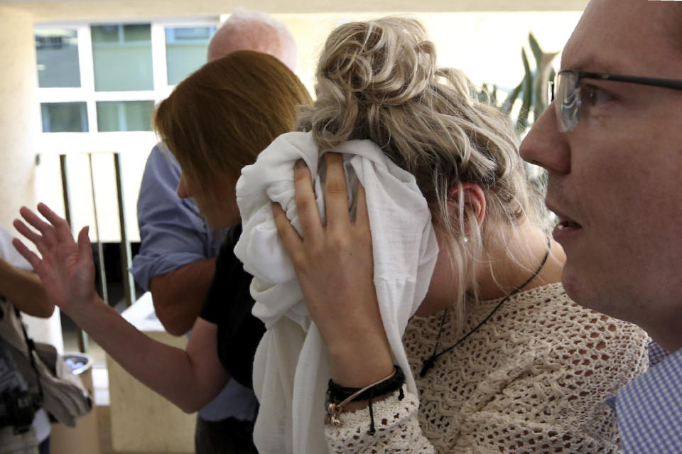 A 19-year old British woman, center, covers her face as she arrives at the Famagusta court for the first day of her trial, in Paralimni, Cyprus, Wednesday, Oct. 2, 2019. The 19 year old British woman pleaded not guilty to making up an accusation that she was raped by a dozen Israelis at a hotel in a Cypriot resort town. (AP Photo/Petros Karadjias)