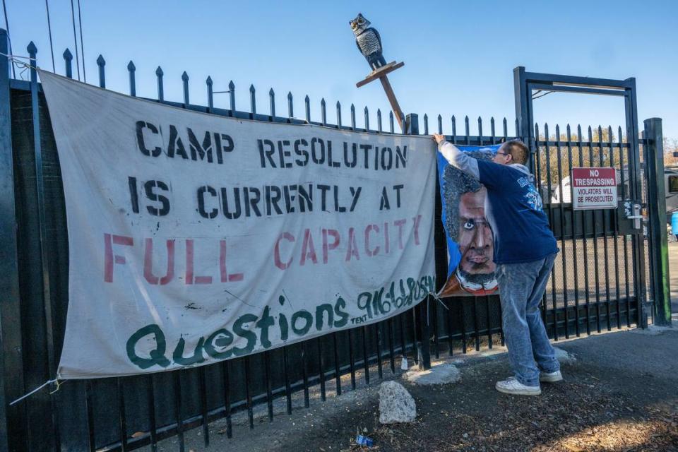 Sharon Jones adjusts a banner Wednesday, Dec. 13, 2023, outside the security gate of Camp Resolution, a self-governing homeless encampment she co-founded with her wife Joyce Williams on a lot they leased from the city of Sacramento in April. They said there is a waiting list of 800 people to get into the camp, which is full to capacity. “We need to pull the homeless into camps or put them in housing,” said Jones.