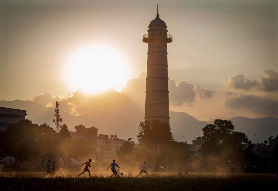 People play football at Tundikhel as Dharahara tower is seen in the background in Kathmandu, Nepal, Wednesday, Nov. 9, 2022.