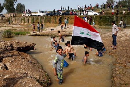A boy holds the Iraqi flag as he plays in the water with other children during a Friday holiday at Shallalat district (Arabic for "waterfalls") in eastern Mosul, Iraq, April 21, 2017. REUTERS/Muhammad Hamed
