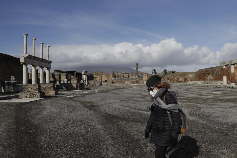 Clouds hang over the Vesuvius volcano, background, as a woman walks in the Forum of the archeological site of Pompeii, southern Italy, during the inauguration of the museum Antiquarium, Monday, Jan. 25, 2021. Decades after suffering bombing and earthquake damage, Pompeii's museum is back in business, showing off exquisite finds from excavations of the ancient Roman city. Officials of the archaeological park of the ruins of the city destroyed in 79 A.D. by the eruption of Mount Vesuvius inaugurated the museum on Monday. (AP Photo/Gregorio Borgia)