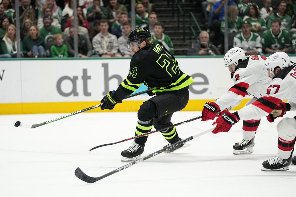 Dallas Stars center Roope Hintz (24) flips a shot at the net after getting past New Jersey Devils defenseman Nick DeSimone (57) and Brendan Smith (2) in the first period of an NHL hockey game in Dallas, Thursday, March 14, 2024. (AP Photo/Tony Gutierrez)