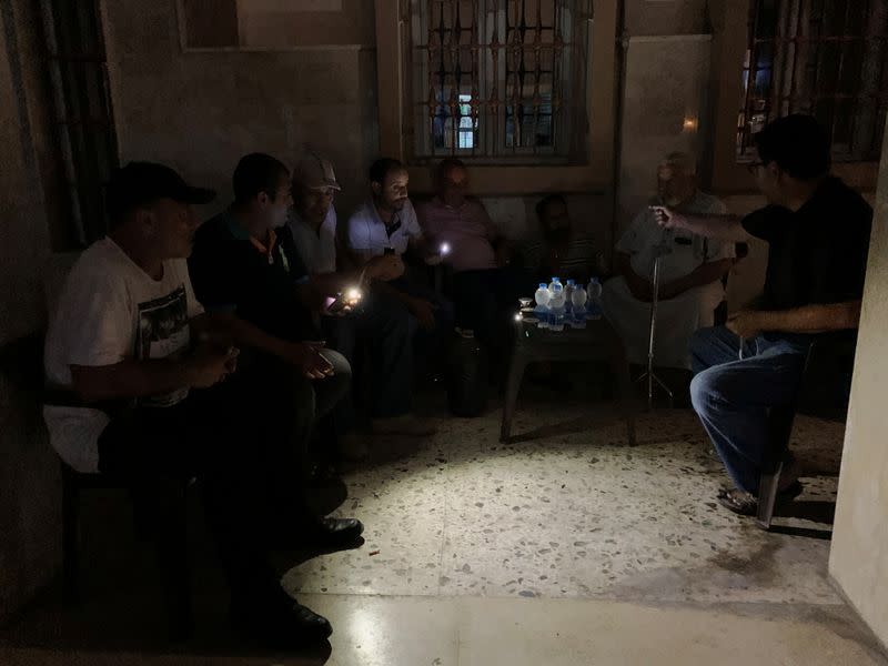 Men sit at a cafe using their phones to light up during a power cut following the long-lasting blackouts, in Misrata