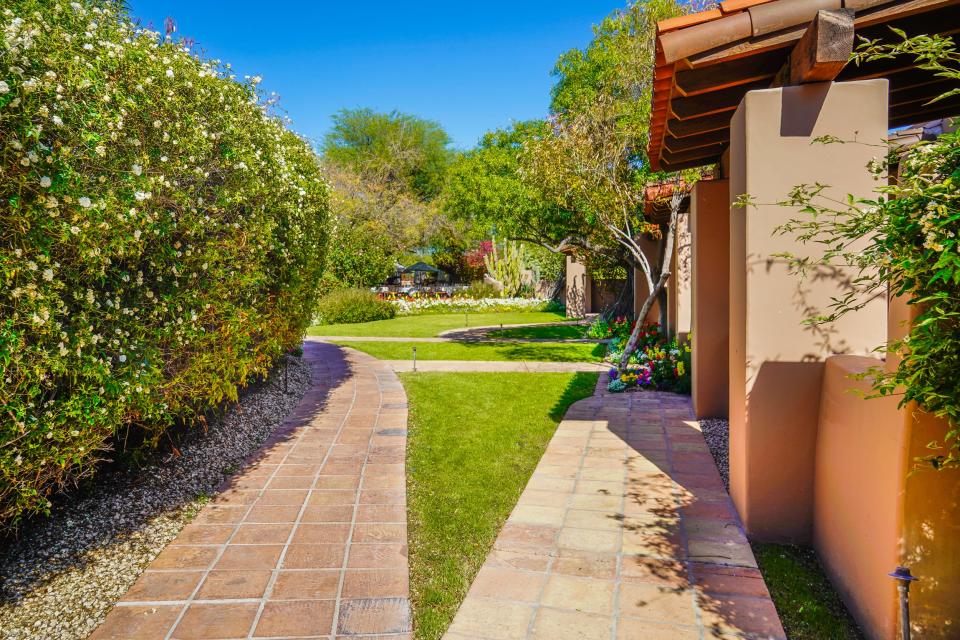 A split pathway in a garden witth a bush on the left, adobe buildings on the right, and flowers and cacti in the distance in the center at Hermosa Inn