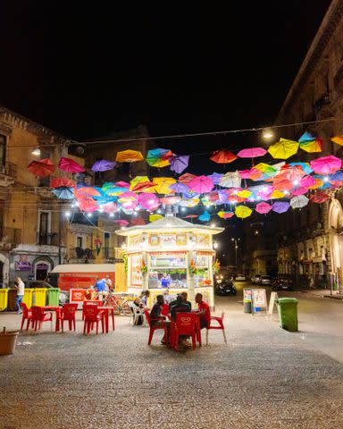 <p>Cedric Angeles</p> Customers enjoy a limone seltzer under umbrellas in a piazza in Catania