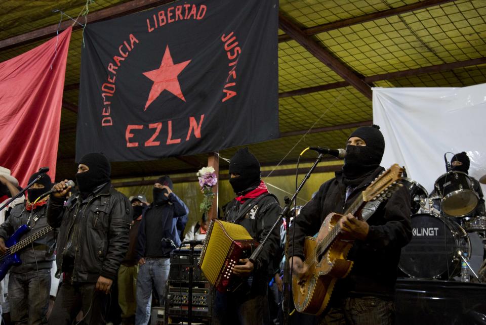 Masked members of the Zapatista National Liberation Army, EZLN, sing the Zapatista hymn under a Zapatista flag that reads in Spanish "Democracy, Liberty, Justice" at an event marking the 20th anniversary of the Zapatista uprising in the town of Oventic, Chiapas, Mexico, late Tuesday, Dec. 31, 2013. In the misty mountain strongholds of the southern Mexico state of Chiapas, ski-mask-clad members and supporters of the Zapatista rebel movement gathered to mark the 20th anniversary of a New Year’s uprising that wrenched the world’s attention to the plight of the country’s impoverished and oft-ignored Indians. (AP Photo/Eduardo Verdugo)