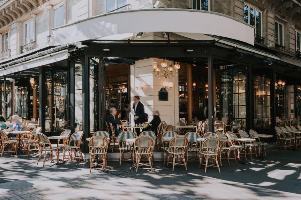 Exterior of a french cafe with tables and chairs set up for dining on the sidewlk