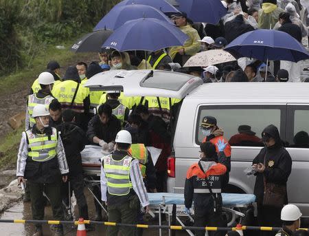 ATTENTION - VISUAL COVERAGE OF SCENES OF INJURY OR DEATH Emergency personnel prepare to transport a body a passenger who died in the TransAsia Airways Flight GE235 plane crash as family members of the passengers (back with umbrellas) wait in New Taipei City February 6, 2015. REUTERS/Pichi Chuang