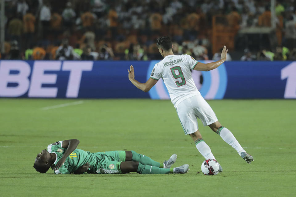 Algeria's Baghdad Bounedjah ,right, gestures as Senegal's Ismaila Sarr lays on the pitch during the African Cup of Nations final soccer match between Algeria and Senegal in Cairo International stadium in Cairo, Egypt, Friday, July 19, 2019. (AP Photo/Hassan Ammar)