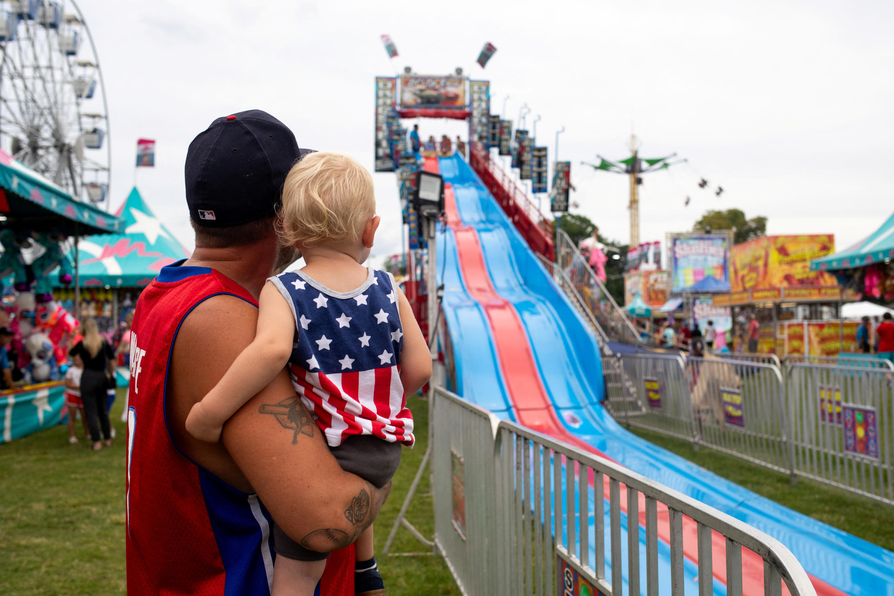 Steven Beaubien holds his toddler son, Silas Beaubien, as they watch people go down a slide at an annual carnival in Clawson, Mich., to celebrate the Fourth of July.