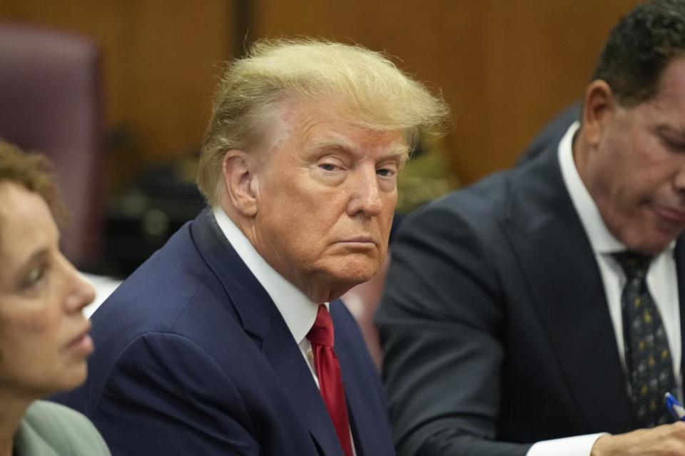 Donald Trump sits in a courtroom in a navy suit and red tie.