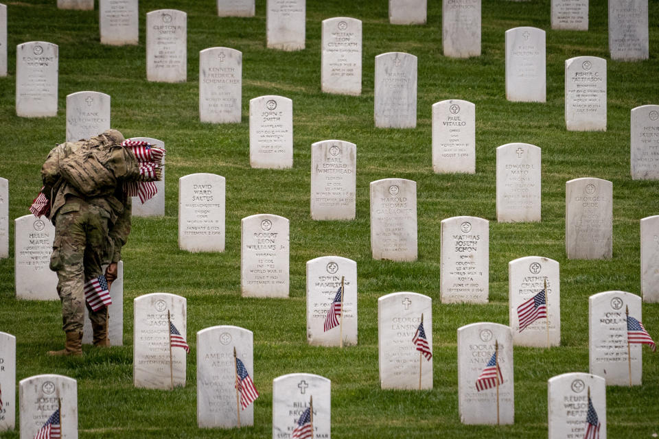 A member of the 3rd U.S. Infantry Regiment also known as The Old Guard, places flags in front of each headstone for "Flags-In" at Arlington National Cemetery in Arlington, Thursday, May 25, 2023, to honor the Nation's fallen military heroes ahead of Memorial Day. (AP Photo/Andrew Harnik)