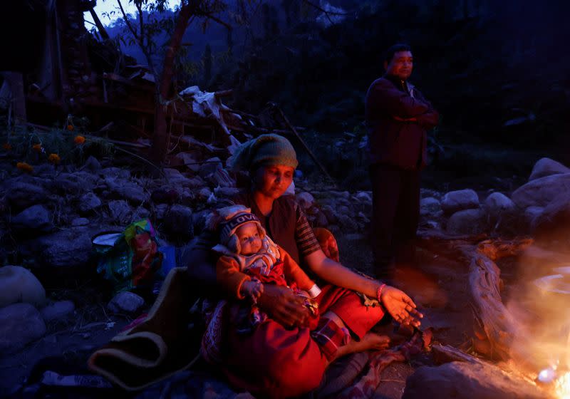 A woman holding a child sits next to the fire to keep warm early in the morning after spending the night out in the open after an earthquake in Rukum