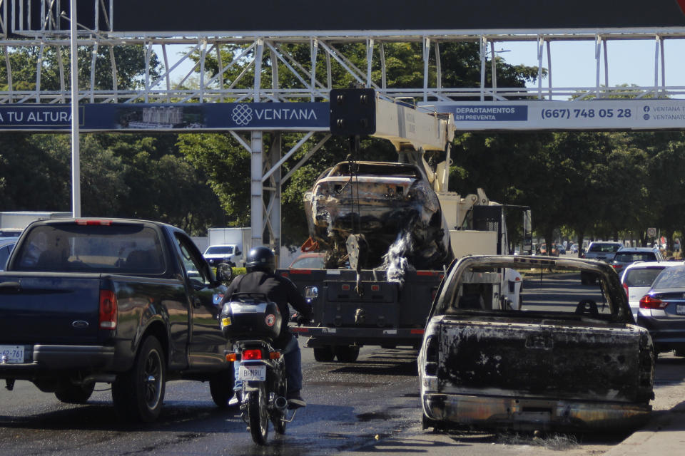 Traffic drive past a charred vehicle set on fire the day before, in Culiacan, Sinaloa state, Mexico, Friday, Jan. 6, 2023. The government operation on Thursday to detain Ovidio Guzman, the son of imprisoned drug lord Joaquin "El Chapo" Guzman, unleashed firefights that killed 10 military personnel and 19 suspected members of the Sinaloa drug cartel, according to authorities. (AP Photo/Martin Urista)