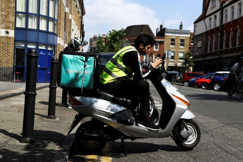 FILE PHOTO: A Deliveroo scooter driver takes a break between deliveries in London