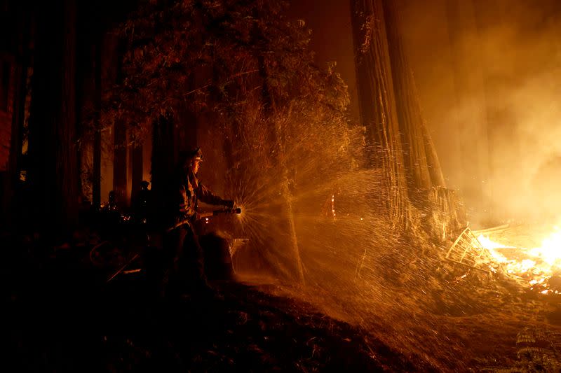 El bombero de Cal Fire Anthony Quiroz rocía agua sobre una llama mientras defiende una casa durante incnedio en Boulder Creek, California