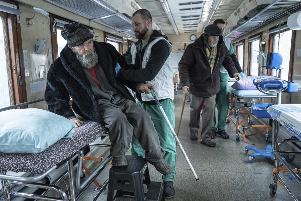 MSF workers help elderly men to take their seats inside MSF medical train that evacuates patients from near the frontlines of the fighting to safer areas at the train station in Pokrovsk, Ukraine, Tuesday, Feb. 14, 2023. (AP Photo/Evgeniy Maloletka)
