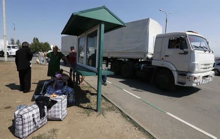 Trucks of a Russian convoy carrying humanitarian aid for Ukraine drive onto the territory of Russia-Ukraine border crossing point "Donetsk", with people who have fled from fighting in eastern regions of Ukraine seen nearby, in Russia's Rostov Region, August 22, 2014. REUTERS/Alexander Demianchuk